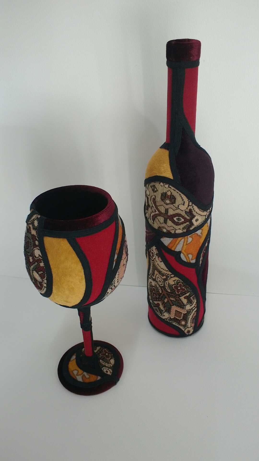 Sculpture 'A Good Drop' by Libby Bloxham. A wine bottle and wine glass are covered in swatches of various fabrics. The fabric covering is segmented into irregular panels with thick black binding, complimenting the contours of the shapes.