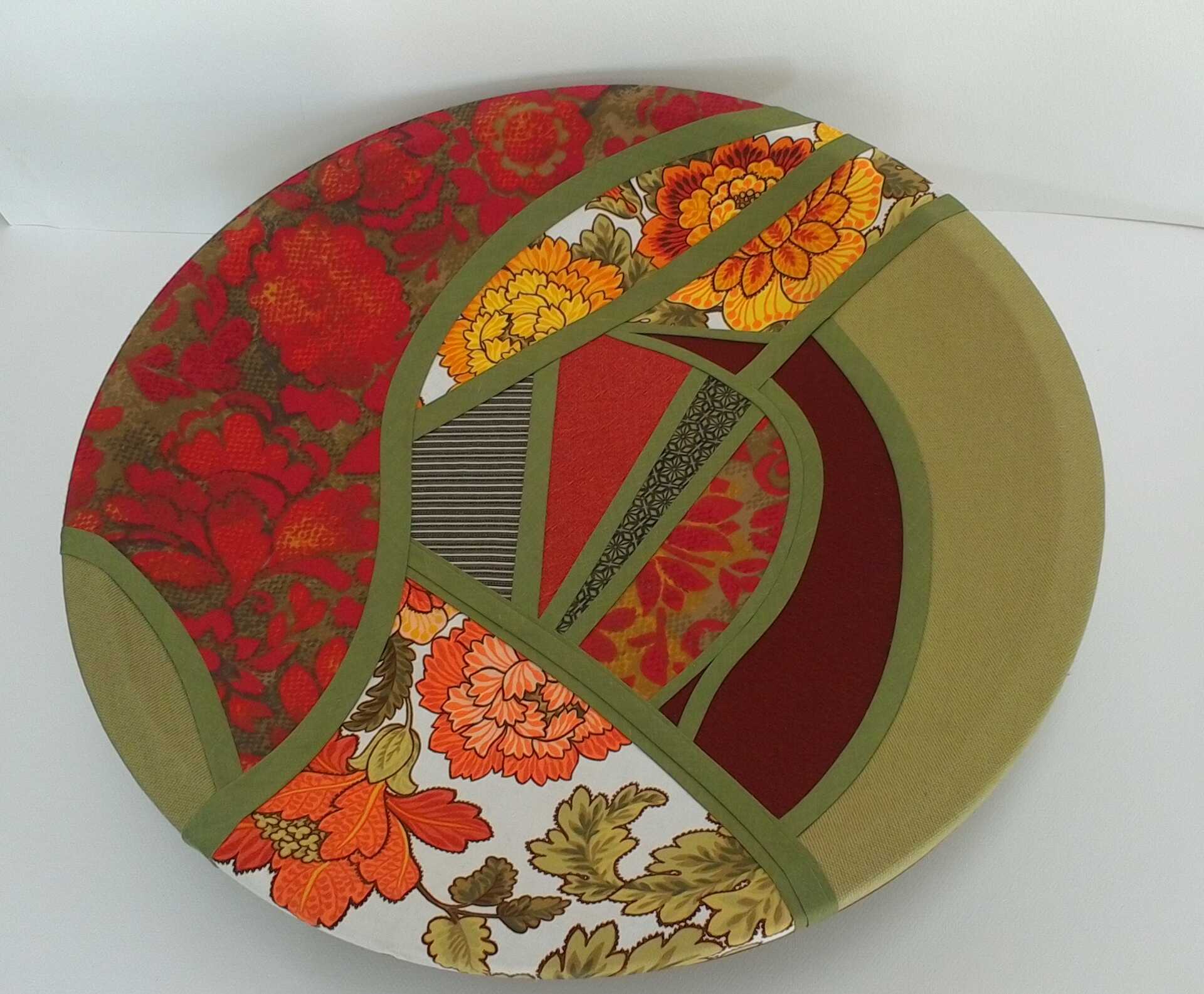 Sculpture 'A Dish to Share' by Libby Bloxham. A round dinner plate is covered in swatches of fabric favouring olive green and orange tones. The fabric covering is segmented into irregular panels with thick olive green binding, complimenting the contours of the shape.