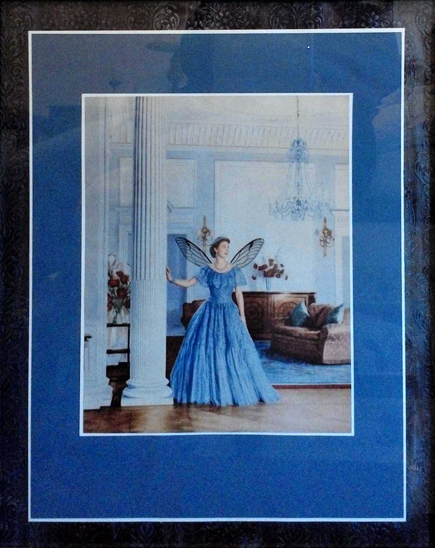 Collage work "Elizabeth" by Libby Bloxham. A layered border of navy blue embossed material and royal blue matte board frames an illustration of a young Queen Elizabeth II, wearing a blue gown as she stands by a white column in a siting room. Acetate insect wings have been positioned at her shoulders.